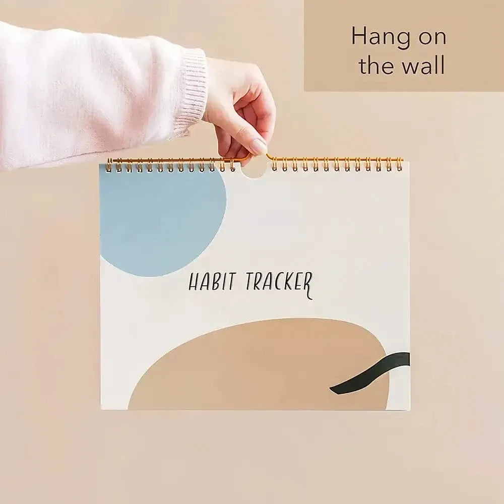 Hand holding a spiral-bound habit tracker planner by the hanging loop for display
