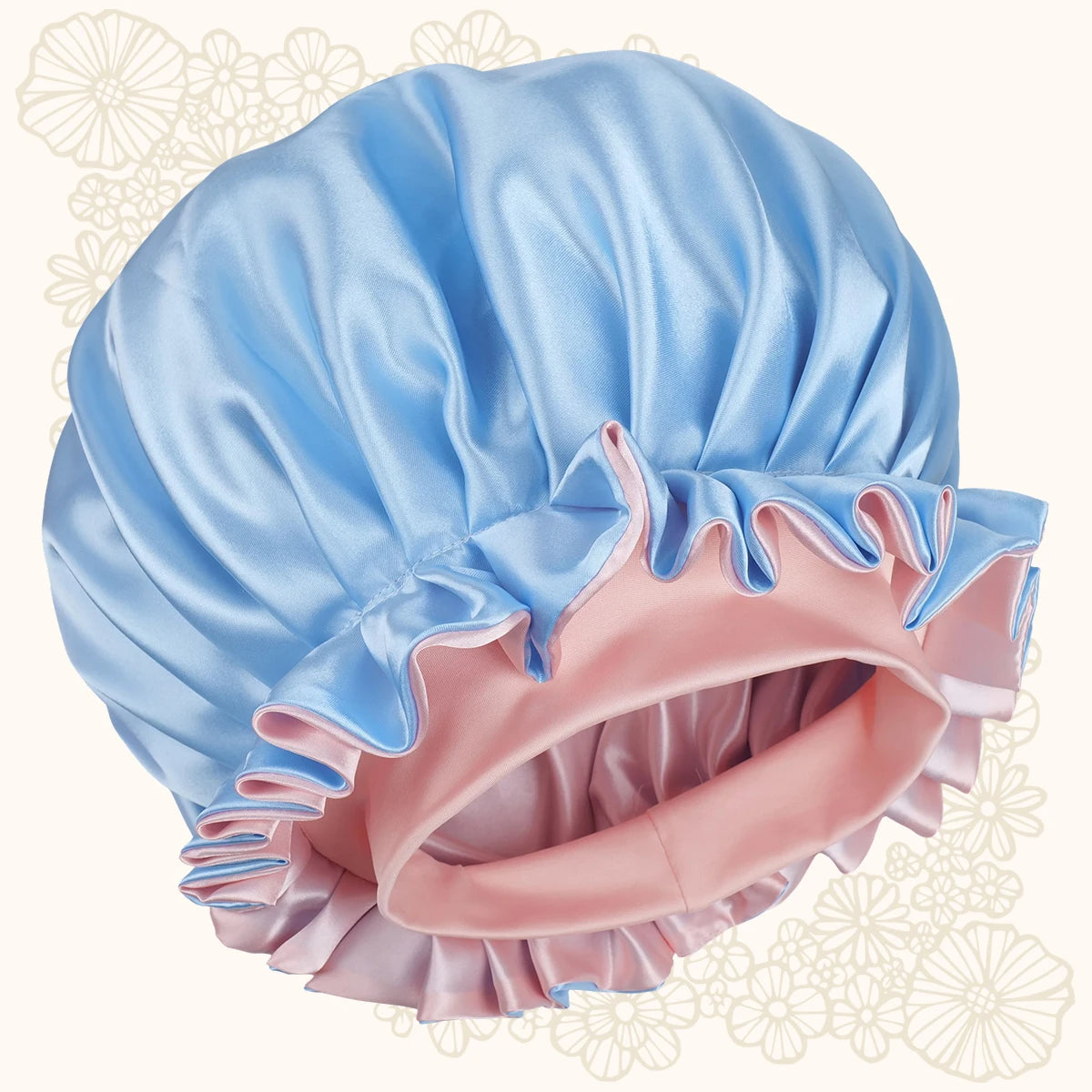 A satin bonnet with a light blue outer layer and a pink inner layer, featuring ruffled trim, shown against a cream background with subtle floral patterns.