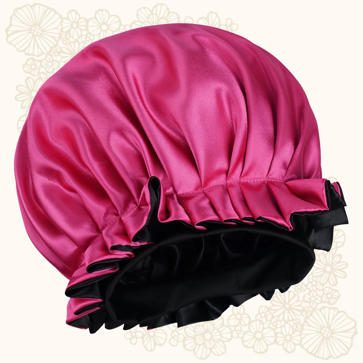 A satin shower cap in vibrant magenta pink with a black ruffled trim and black inner lining, shown against a light cream background with subtle floral patterns.