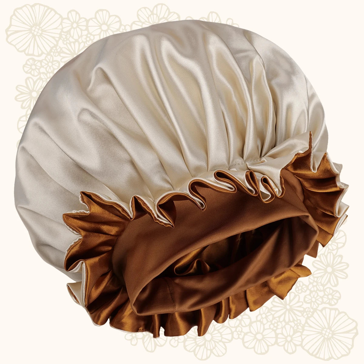 A satin bonnet with a cream-colored upper section and a brown ruffled trim along the lower edge, shown against a light cream background with faint floral patterns.