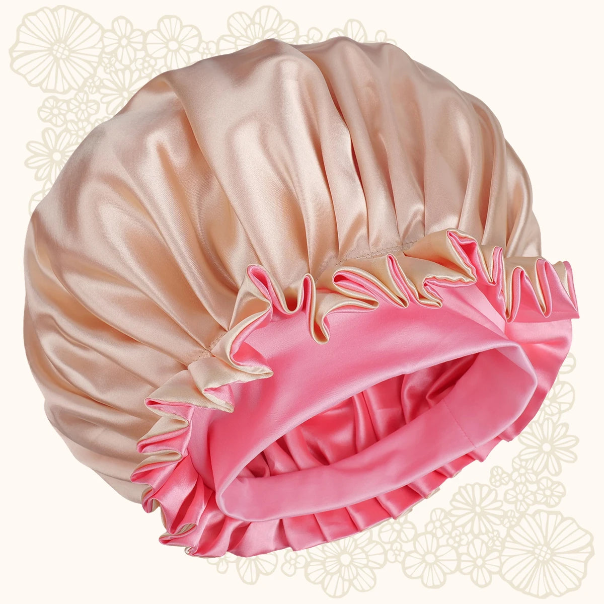 A satin bonnet with a pleated ruffled trim, featuring a light peach-beige main body and a contrasting bright pink inner band, set against a cream background with faint floral patterns.
