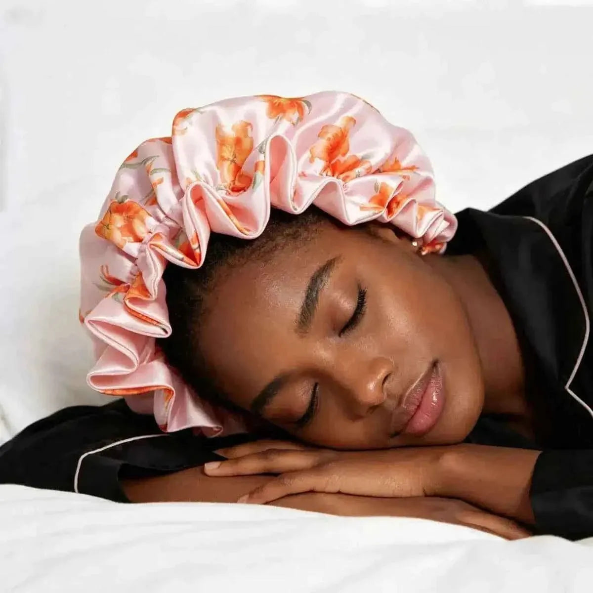 Women's satin hair bonnet in pink with orange floral print, worn on head with ruffled crown